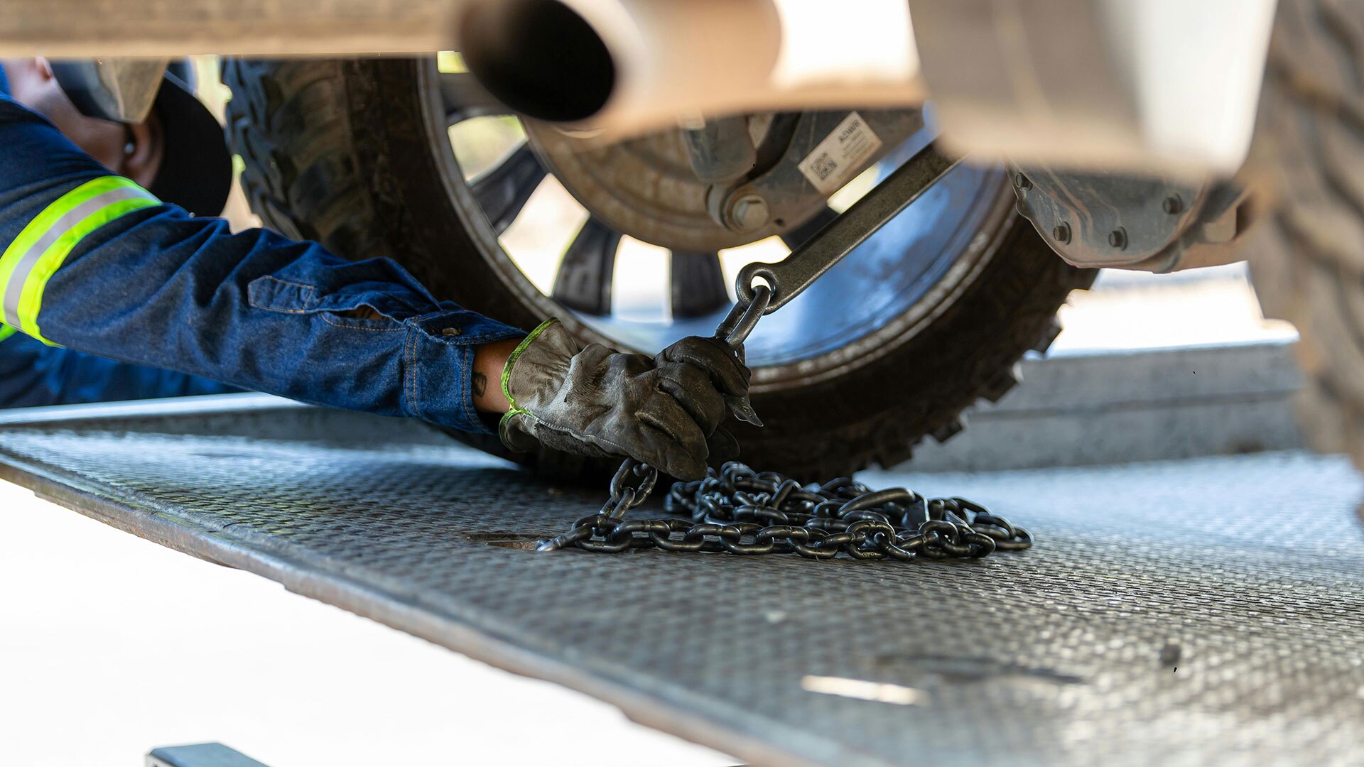 A tow truck driver attaches the bottom of a car to the truck with a chain.