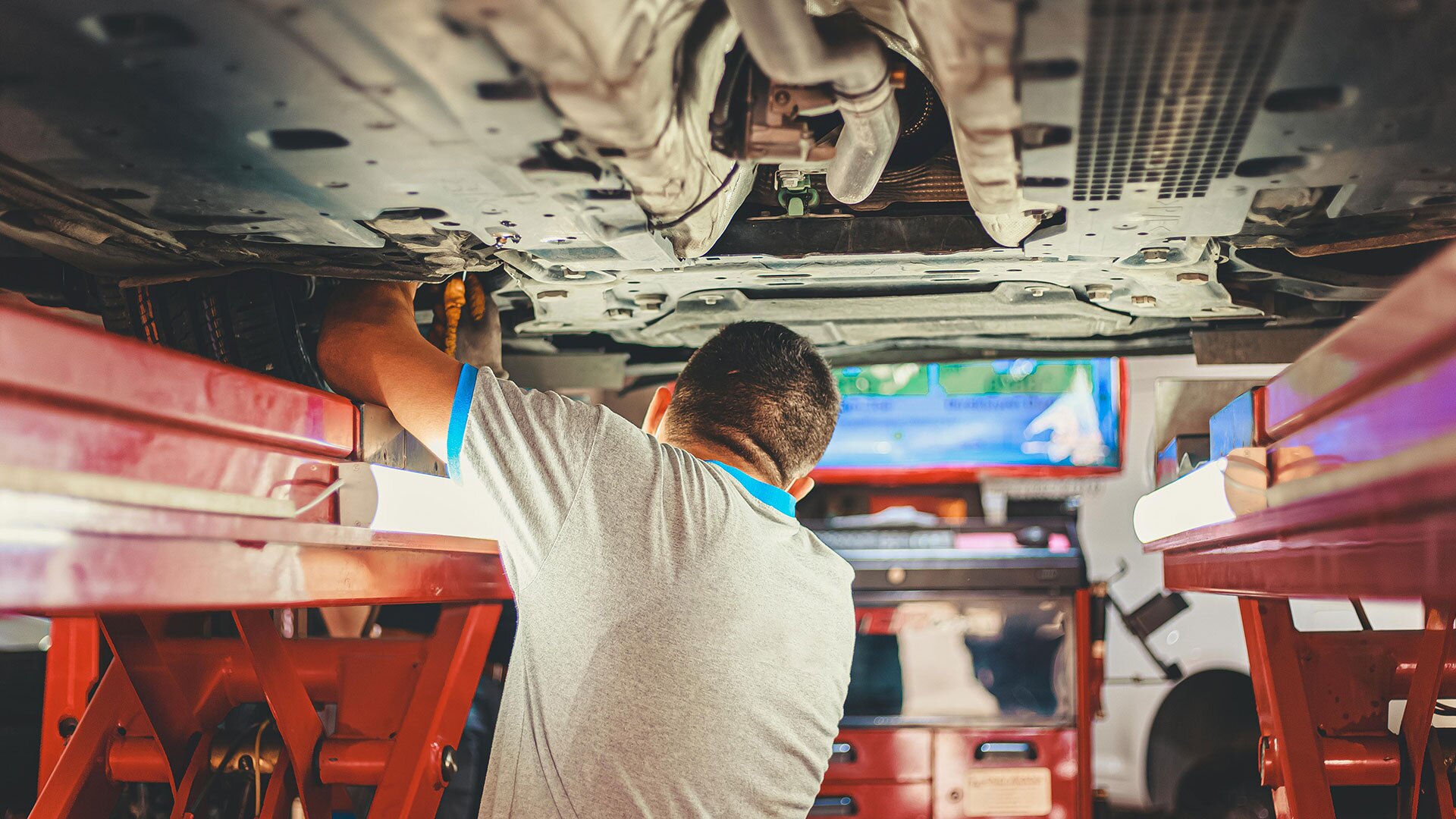 A mechanic works on the underside of a car.