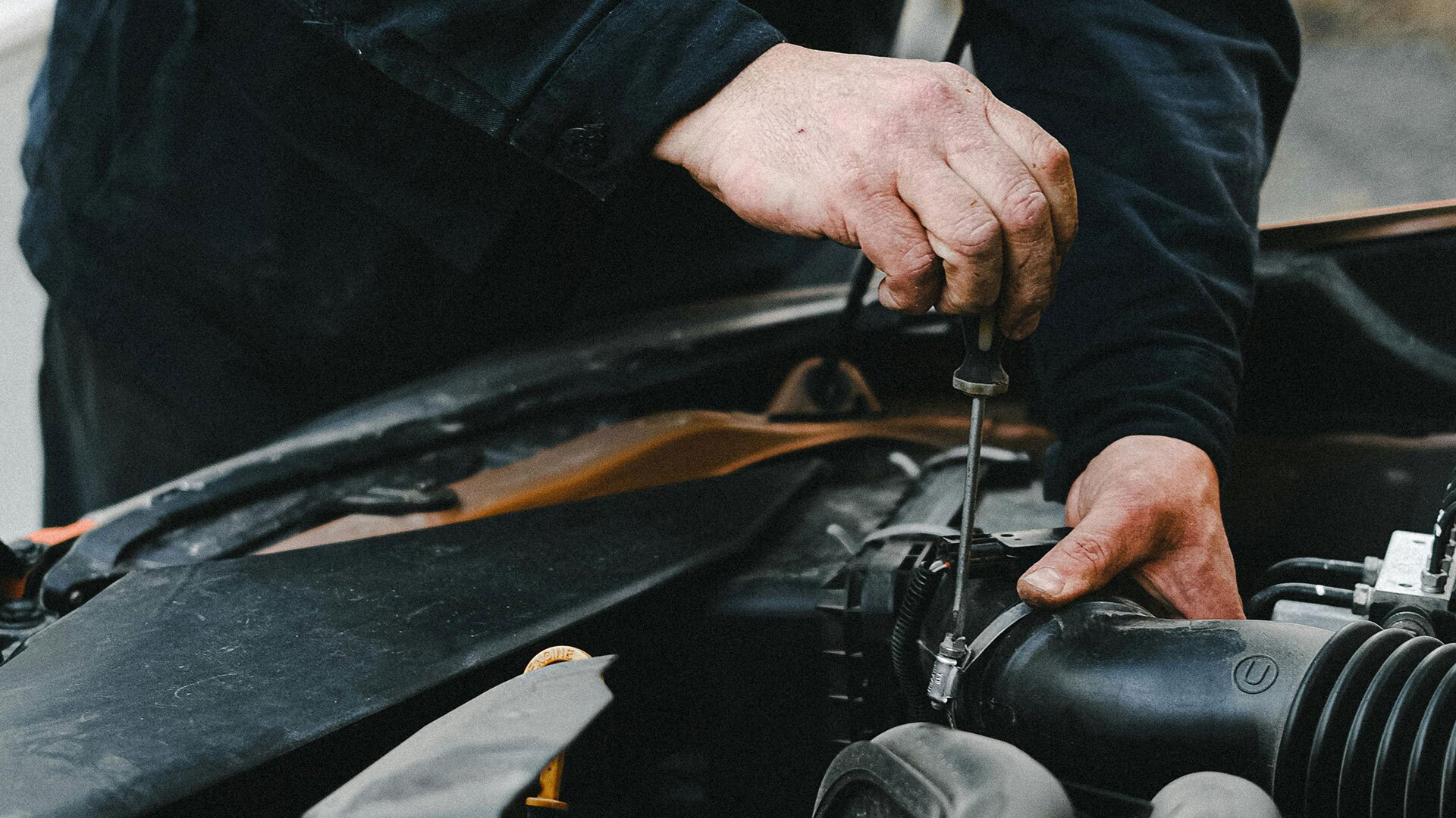 A person makes some engine repairs with a screwdriver.